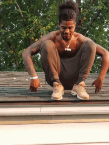 a shirtless man squatting on a roof with a necklace that says fox on it