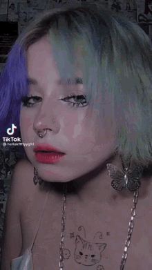 a woman with purple and green hair has a cat tattoo on her chest