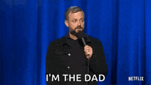 a man with a beard is holding a microphone on a stage and saying `` i 'm the dad '' .