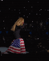 a woman in a black jumpsuit singing into a microphone while standing on an american flag