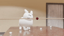 a white stuffed animal is laying on a table with a red ball in its mouth