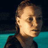 a close up of a woman 's face in front of a pool at night