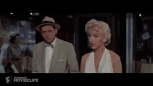 a woman in a white dress is standing next to a man in khaki pants and a fandango movieclips logo