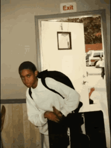 a boy with a backpack stands in front of an exit sign