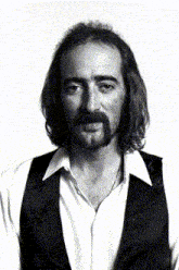 a man with long hair and a beard wears a black vest