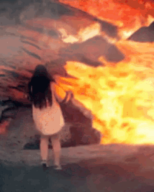 a woman in a white dress is standing in front of a fire