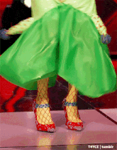 a woman wearing a green skirt and red shoes is dancing on a dance floor