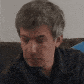 a man with gray hair is sitting on a black couch with his eyes closed