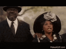 a man in a suit and tie stands next to a woman in a black hat .
