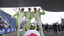three men in green and white racing suits are standing next to each other in front of a sign that says 2h