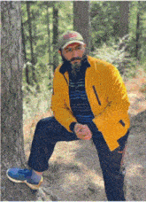 a man in a yellow jacket sits on a tree trunk in the woods