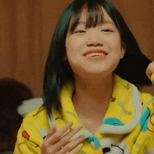 a young girl with green hair is wearing a yellow pajama top and smiling .
