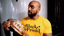 a man wearing a yellow shirt that says black and proud is holding a belt