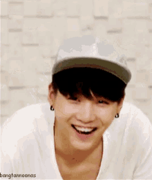 a young man wearing a baseball cap and a white shirt smiles