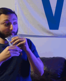 a man with a beard is drinking from a glass in front of a blue v