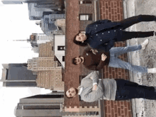 three people are posing for a picture on top of a building in front of a city skyline .