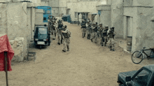 a group of soldiers are walking down a dirt street in a city .