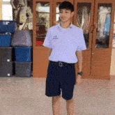 a boy wearing a white shirt and black shorts is standing in front of a cabinet