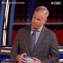 a man in a suit and tie is holding a football that says family feud canada on it