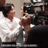 a man in a white shirt is talking to another man while a cameraman takes a picture of him