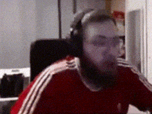 a man with a beard is sitting in a chair wearing headphones and a red shirt .
