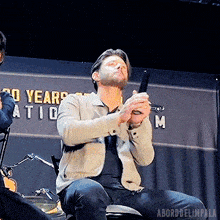 a man is sitting on a stage holding a gun in front of a sign that says 20 years