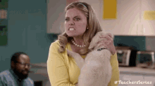 a woman in a yellow sweater is holding a puppy in her arms and making a funny face .