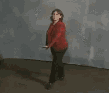 a woman in a red shirt and black pants is dancing in a room with her arms outstretched .