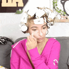 a woman with curlers on her head is wearing a pink sweatshirt with a heart on it