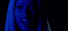 a close up of a woman 's face in a dark room with a blue background .