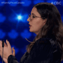 a woman wearing glasses applauds while standing in front of a microphone with the hashtag familyfeud canada