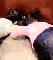 a woman in a pink sweater is laying on the floor next to a dog .