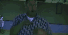 a man in a striped shirt is standing in a dark room with a red exit sign in the background