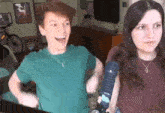 a man and a woman are standing next to each other in a living room . the man is wearing a green shirt .