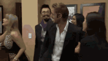 a group of people are standing in a room and one of them is wearing a suit