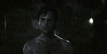 a man without a shirt is standing in a dark room with a candle in the background .