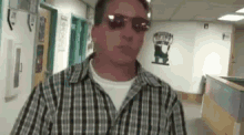 a man wearing sunglasses and a plaid shirt is standing in a hallway
