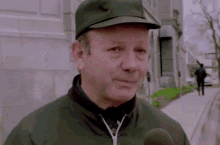a man wearing a hat and jacket is talking into a microphone
