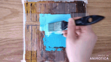 a person is using a brush to paint a blue square on a wooden surface made in animatica