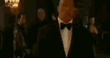 a man in a tuxedo and bow tie is holding a piece of paper in his hands .