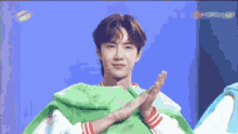 a man wearing a green sweater is making a cross with his hands