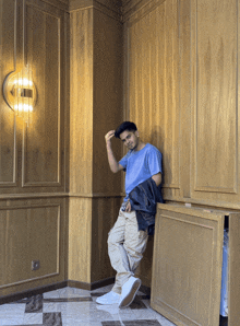 a young man leaning against a wooden wall with a camera in his hand