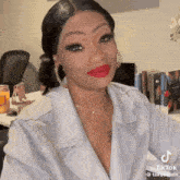 a woman wearing a white jacket and red lipstick is sitting at a table .
