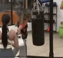 two women are boxing in a gym with a punching bag hanging from the ceiling .