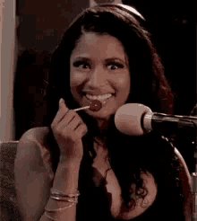 a woman is eating a lollipop in front of a microphone while smiling .