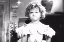 a little girl in a white dress is standing in front of a mirror .