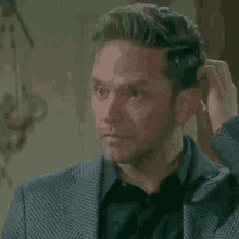 a man in a suit and black shirt is touching his hair .