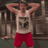 a man in a white tank top and red shorts is standing with his hands on his head