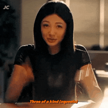 a woman is sitting at a table and says three of a kind squeals