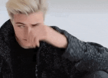 a man is covering his nose with his hand while wearing a black jacket .